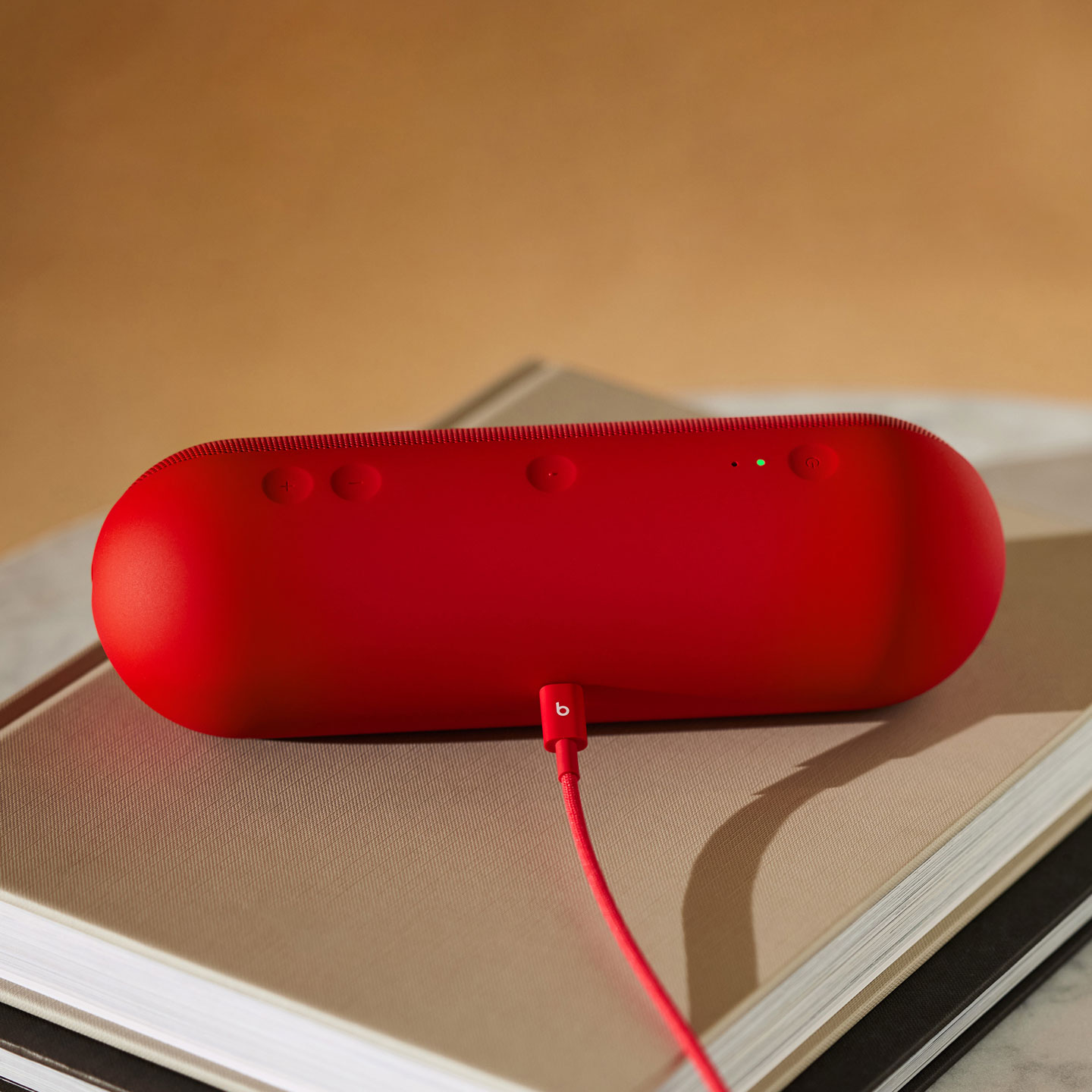 Beats USB-C to USB-C Woven Cable in Rapid Red plugged into a Beats Pill in Statement Red. 